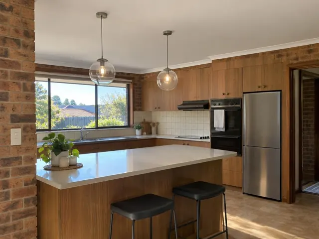 Kitchen with two glass pendant lights over an island, wood cabinetry and brick walls in Bonnells Bay
